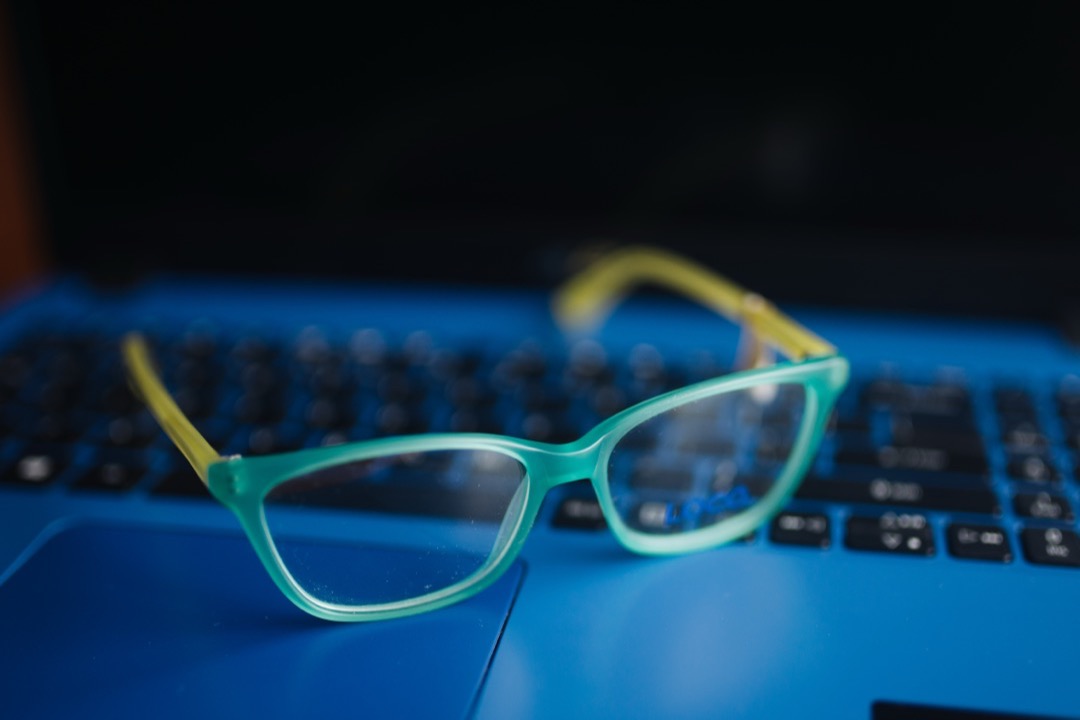 Teal blue light glasses resting on a blue laptop keyboard