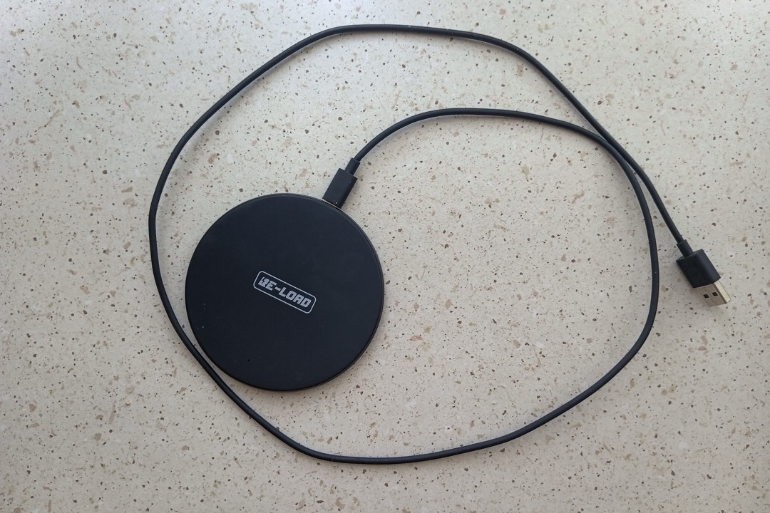 A round black Qi wireless charging pad with its cable on a speckled desk surface
