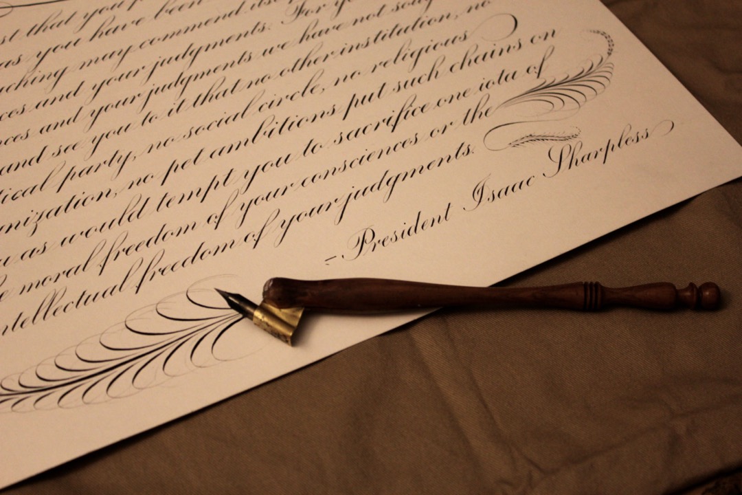 A finished sheet of Copperplate calligraphy with an oblique wooden penholder and brass flange resting on top of it