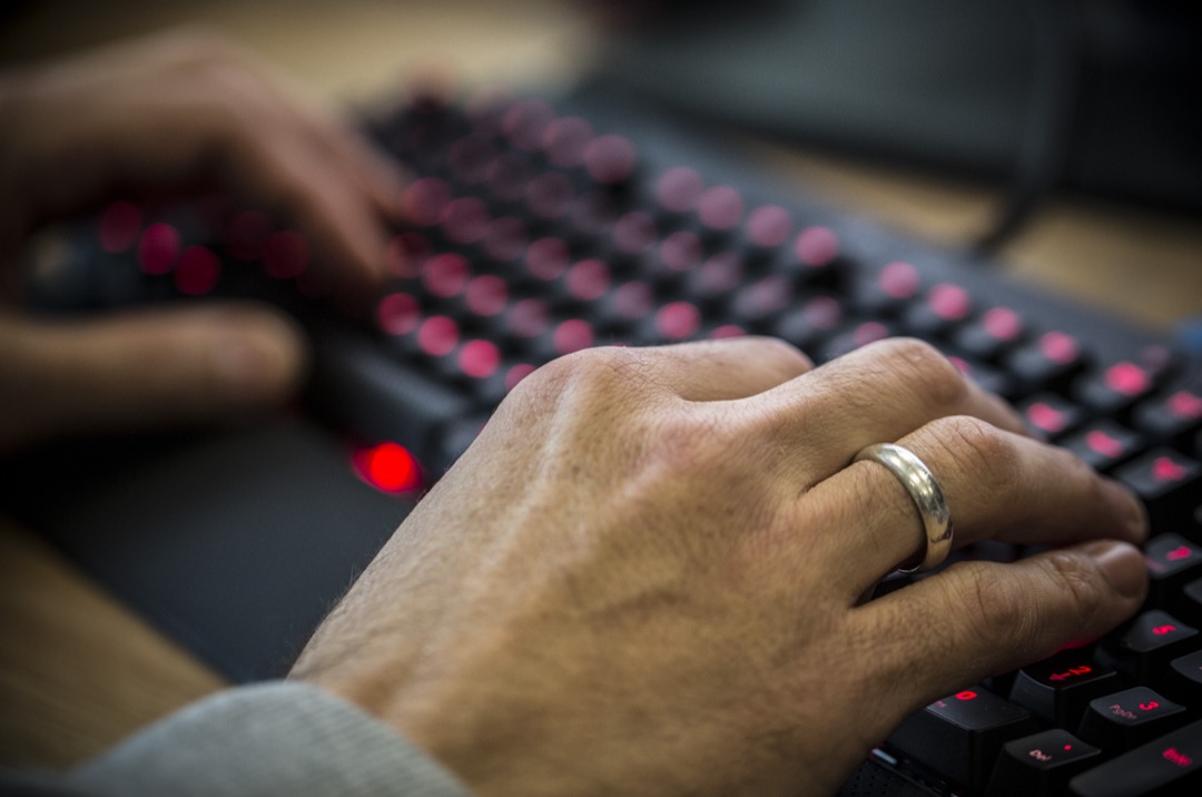Two hands typing on a black mechanical keyboard with red backlighting, forearms resting on a padded rest at the desk edge