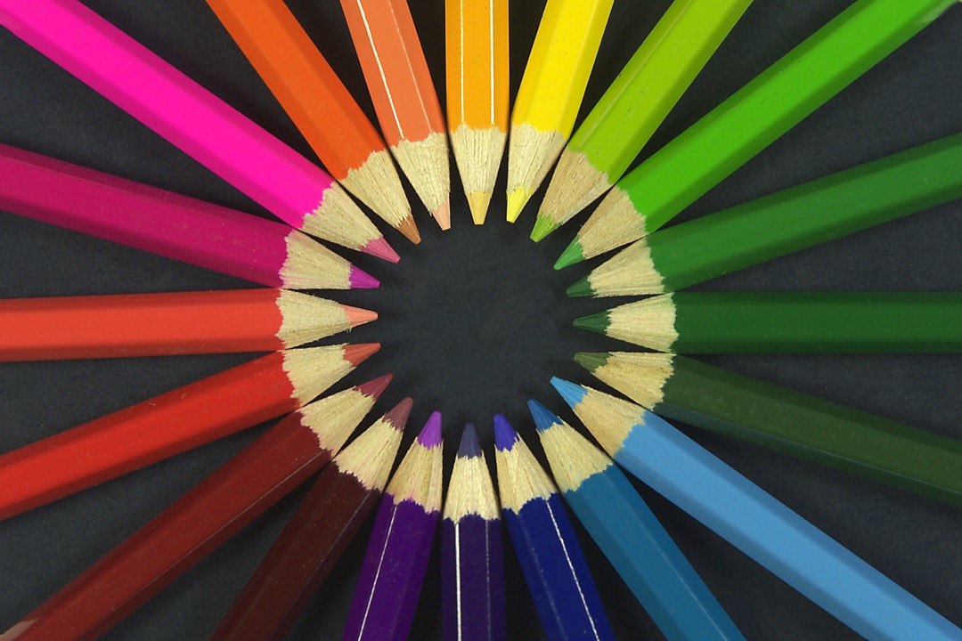 A set of colored pencils arranged in a fan on a white desk surface