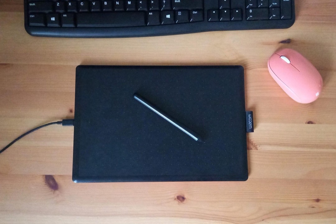 An organized minimalist desk with a laptop, notebook, pen cup, and small plant on a clean wooden surface