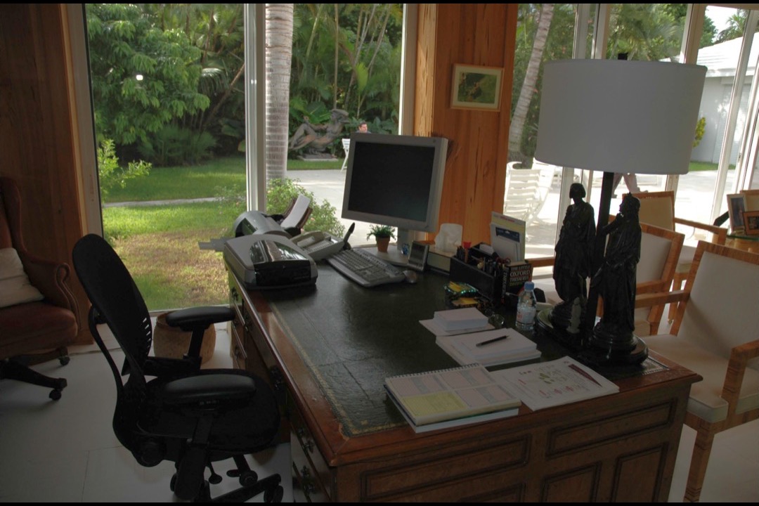 A wooden home office desk with an adjustable task lamp beside a bright window