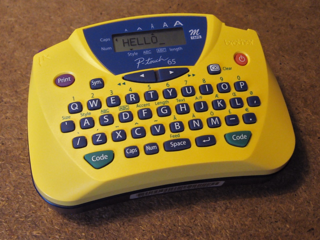 A yellow Brother P-touch label maker with a QWERTY keyboard and the word HELLO typed on its display