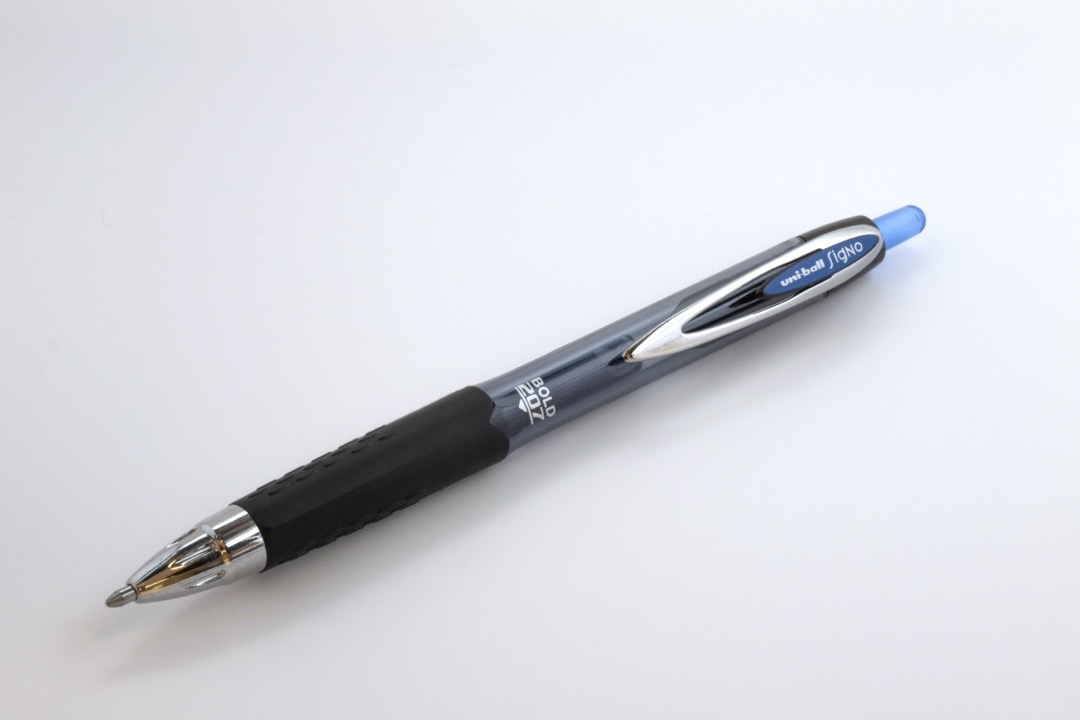 Pilot G2 and Uni-Ball Signo gel pens laid side by side on a white desk surface